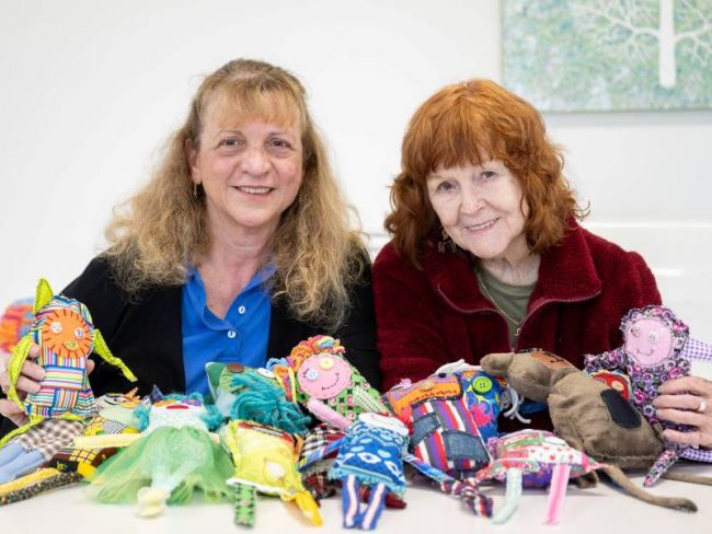 Two volunteers holding hand-made soft toy dolls