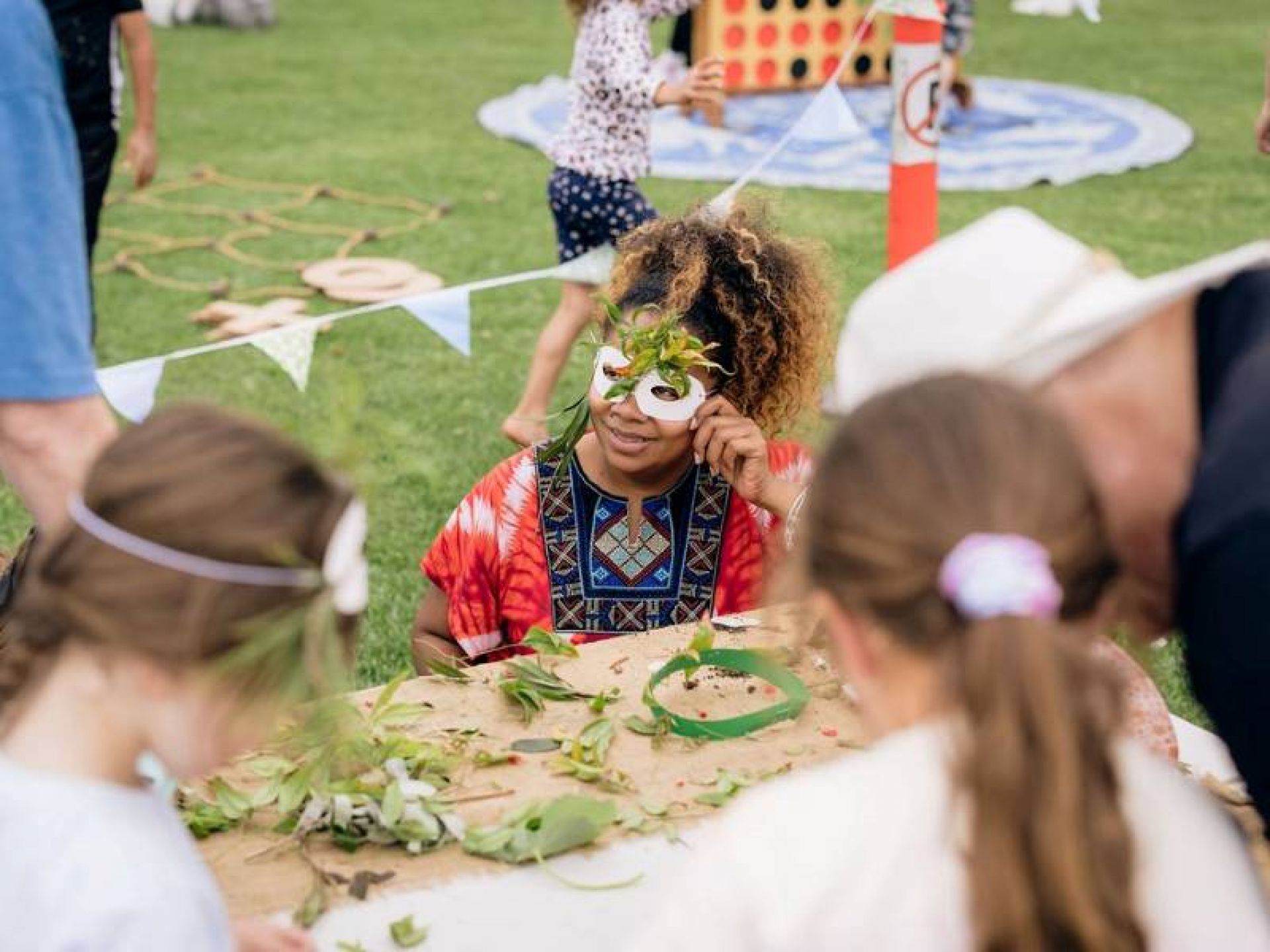 Young child holding a mask decorated with leaves to their face