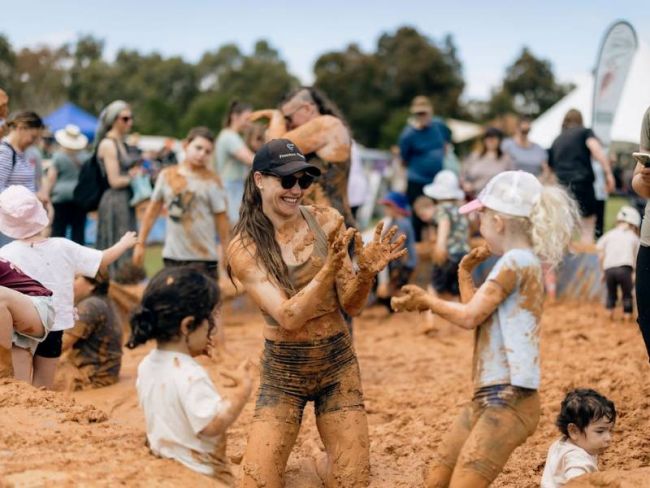 Adult and children playing in a large mud pit