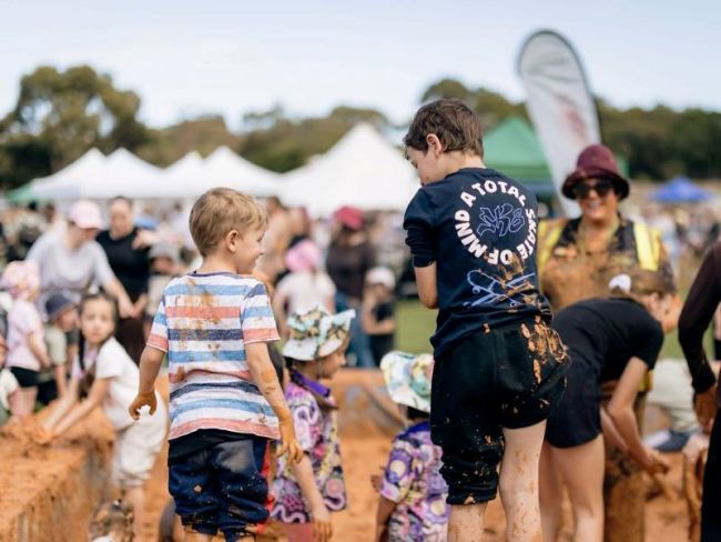 Young children laughing while playing in a large mud pit