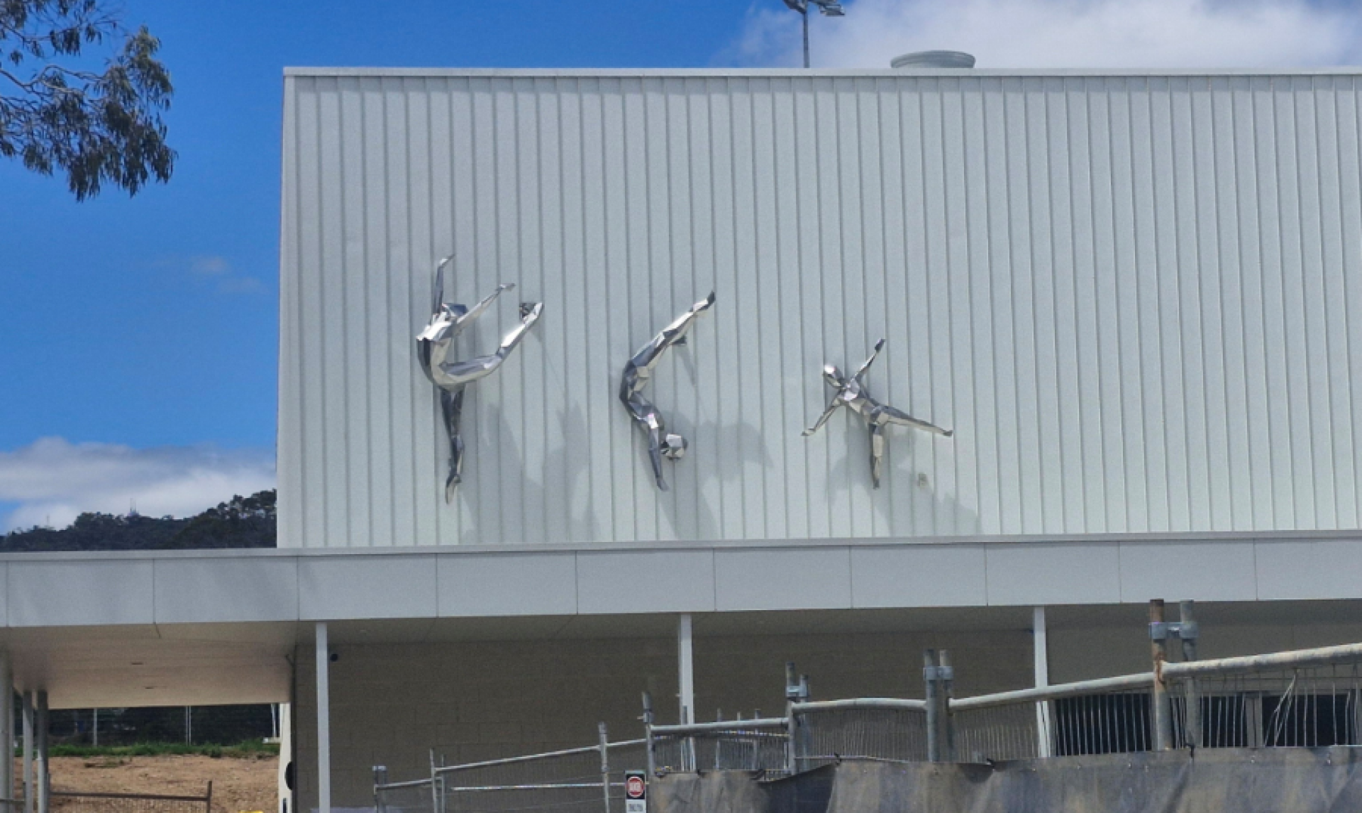 Three sculptures of gymnasts in dynamic poses on building exterior