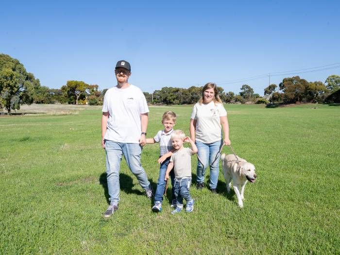 Two adults, two children and a white dog walking across a grassed reserve