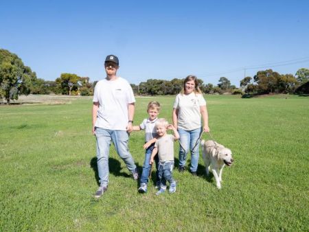 Two adults, two children and a white dog walking across a grassed reserve